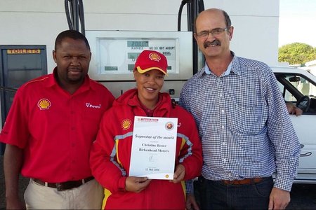 Schalk  Strauss (regs),  bestuurder  van  Birkenhead  Motors,  oorhandig  â€˜n kontantprys  en  sertifikaat  aan  Christine Bester.   Claude  Vanqa,    area-bestuurder van Shell staan by.