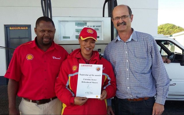 Schalk  Strauss (regs),  bestuurder  van  Birkenhead  Motors,  oorhandig  â€˜n kontantprys  en  sertifikaat  aan  Christine Bester.   Claude  Vanqa,    area-bestuurder van Shell staan by.