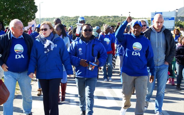 DA-leiers tydens â€˜n vreedsame optog saam met die Wes-Kaapse Premier, Helen Zille met singende en dansende ondersteuners van Masakhane agter hulle.  Voor vlnr is  Rdl Dudley Coetzee (Wyk 11),  Helen Zille,  Masizole Mnqasela (Lid van die Provinsiale Parlement),  Andrew Komani (Wyk 1)  en  dr. Michael Cardo (Lid van die Parlement).