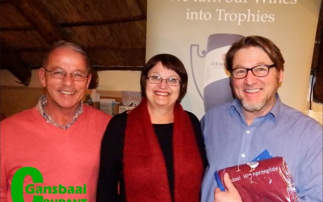 Die aanbieder tydens Gansbaai Wynproegilde se wynproe aand, Andre Rheeder (regs) staan met sy  Wynproegilde voorskoot wat deur klublede Steve Serbon en Anne-Mare de Witt aan hom oorhandig is.