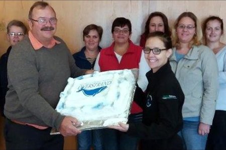 Gilbert (Boetie) Hart se agtiende verjaardagkoek aan Gansbaai Munisipaliteit. Voor hou mnr Kat Myburgh en Tanya Smit die verjaardagkoek vas. Agter vlnr Annelie Lourens, Carol Devitt, Sanet Otto, Junita Booker, Louise Groenewald, Annemien van der Merwe, Vanessa Ventura, Marissa Radyn en Philip Fourie.