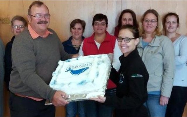 Gilbert (Boetie) Hart se agtiende verjaardagkoek aan Gansbaai Munisipaliteit. Voor hou mnr Kat Myburgh en Tanya Smit die verjaardagkoek vas. Agter vlnr Annelie Lourens, Carol Devitt, Sanet Otto, Junita Booker, Louise Groenewald, Annemien van der Merwe, Vanessa Ventura, Marissa Radyn en Philip Fourie.