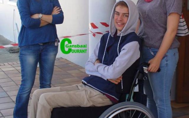 â€˜n Spontane en glimlaggende Calvin Olivier in sy rolstoel tydens â€˜n nootlegging wat ten bate van hom deur Laerskool Gansbaai gereÃ«l is. By hom is sy ma, Denise Olivier (links) en Mikayla Groenewald.