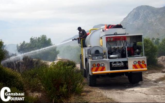 Enkele veldbrande rondom Gansbaai en in die omgewing het weer die afgelope tyd ontstaan.  Hier is Gallie Badenhorst agter die stuur besig terwyl brandweerman Thembelani Xovula probeer om die smeulende veldbrand onder beheer te bring.