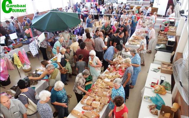 â€˜n Geheelbeeld van die gesellige basaar, met stalletjies in die sy-saal en buite op die terein.