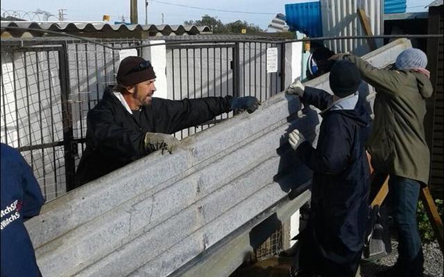 Martin Butler hou een van die groot dakplate vas wat by BARC se hokke afgewaai het, terwyl van die ander helpers aan die anderkant besig is om dit weer reg te buig.