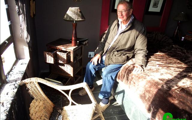 AndrÃ© Vorster sit moedeloos op hulle bed in die roetgevulde slaapkamer, met sy vrou, Judith, se verbrande rottangstoel voor hom en die venstertjie wat uitgeslaan is, skuins bokant die stoel.