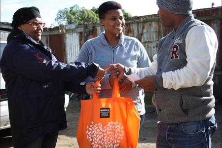 Pinkey Ngewu (DICT) together with Belnay van Tonder (Great White House) handing over a food parcel gift to 1st year DEEP student Vanashree Lotteringâ€™s dad.
