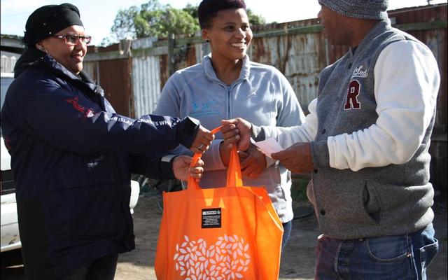 Pinkey Ngewu (DICT) together with Belnay van Tonder (Great White House) handing over a food parcel gift to 1st year DEEP student Vanashree Lotteringâ€™s dad.