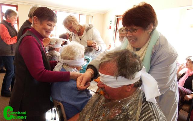 Selfs John van Rooyen, die bestuurder van HaS is geblinddoek vir Goue Hande se item.  Met voorskote gepantser moes die deelnemers raai wat hulle gevoer word.  Die toeskouers het geskaterlag oor die petalje.  Anita Botha (links) en Marie de Jager besig om John se smaakvermoÃ« te toets.