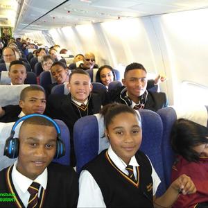 In die vliegtuig, vir almal â€˜n eerste keer, op pad na Johannesburg. Van links: 1ste ry Sebastian Johnson, Daylen Tobias en Kaylin Robertson (klaar aan die slaap!); 2de ry Jaygon Visagie, Izaan Newman en Lorenzo Geldenhuis; 3de ry Ulrich Visagie, SimornÃ© Europa en Heidri Loff; 4de ry regs is Aletta Groenewald (hulp) en Tommy Wilson (skoolhoof).