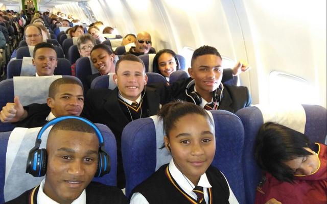 In die vliegtuig, vir almal â€˜n eerste keer, op pad na Johannesburg. Van links: 1ste ry Sebastian Johnson, Daylen Tobias en Kaylin Robertson (klaar aan die slaap!); 2de ry Jaygon Visagie, Izaan Newman en Lorenzo Geldenhuis; 3de ry Ulrich Visagie, SimornÃ© Europa en Heidri Loff; 4de ry regs is Aletta Groenewald (hulp) en Tommy Wilson (skoolhoof).