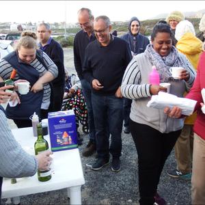 Soos natgereÃ«nde hoenders tydens Gansbaai Toerisme se â€œSunset Walkâ€. Links by die tafel bedien Glenda Kitley en Doulene Els van Gansbaai Toerisme die deelnemers, met Maureen Valentine wat na Sharman Geldenhuys, bibliotekaresse, omsien.