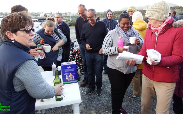 Soos natgereÃ«nde hoenders tydens Gansbaai Toerisme se â€œSunset Walkâ€. Links by die tafel bedien Glenda Kitley en Doulene Els van Gansbaai Toerisme die deelnemers, met Maureen Valentine wat na Sharman Geldenhuys, bibliotekaresse, omsien.