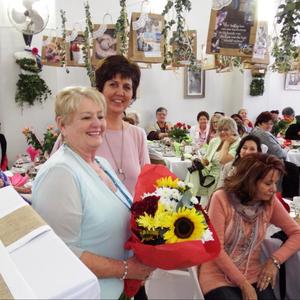 Links voor is past Beryll Coetzer, hooforganiseerder van die damesoggendtee, met die blomme wat Minnette Maree aan haar oorhandig het.