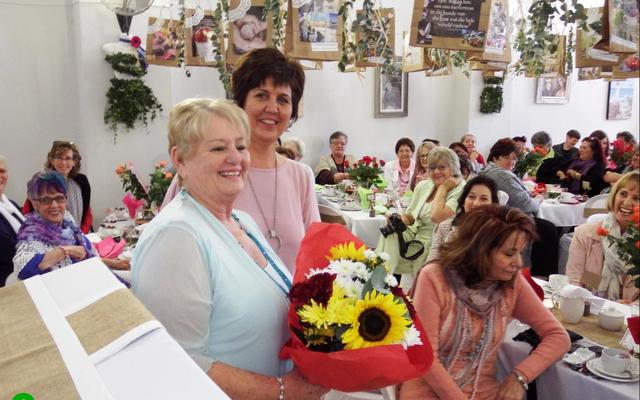 Links voor is past Beryll Coetzer, hooforganiseerder van die damesoggendtee, met die blomme wat Minnette Maree aan haar oorhandig het.