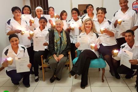 Die tuisversorgers met hul brandende lampies â€“ voor van links: Celeste Dunsdon, Sanna Speelman (beste prestasie: strykwerk), Suster Irene de Waal, El-Marie Fourie (hoogste lof vir teorie en prakties) en Franklin Eksteen (eervolle vermelding).  Agter: CornÃ© Dunsdon (beste blommerangskikking), Trudie Cupedo, Elna Kondokter (prakties en huishouding met lof), Rhowina Kammies, Magdalena Arends (naaldwerktoekenning), Nicole Adonis, Jocoline Louw (slaag prakties met lof), Marlene Gertse (klaskaptein â€“ slaag prakties en tuisversorgingsteorie met lof) en Peter-Lee Karelse (slaag prakties met lof).